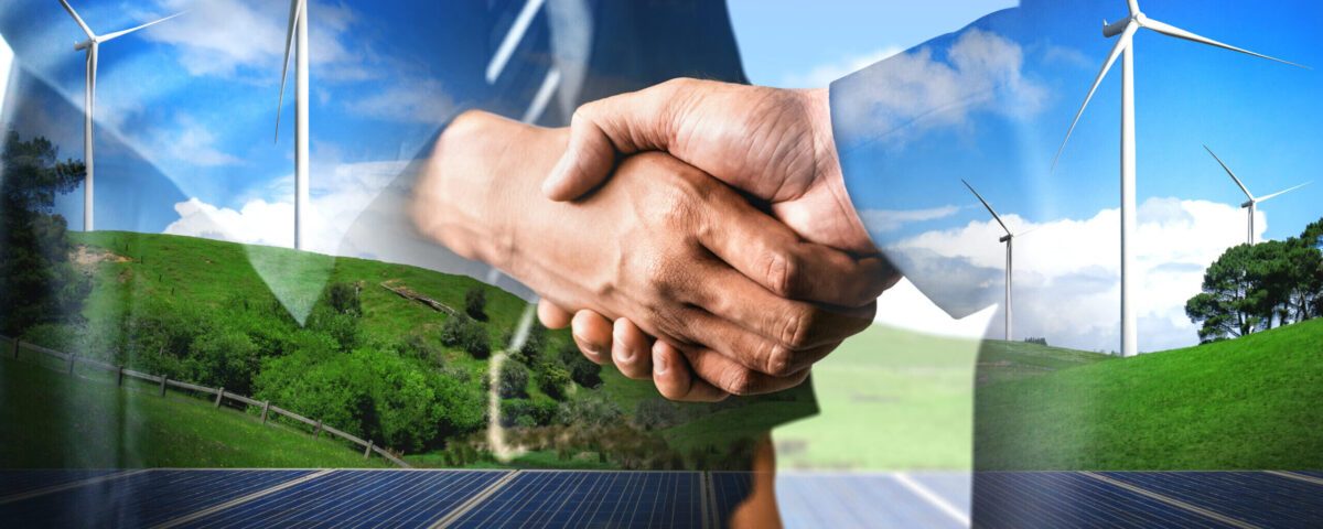 Händedruck vor einer Landschaft mit Windrädern und Solarmodulen